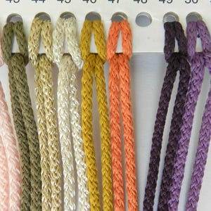 May include: A color chart displaying braided cords in various colors, including olive green, beige, cream, mustard yellow, and orange. The chart also shows cords in shades of purple and brown. Each cord is labeled with a number from 43 to 50.