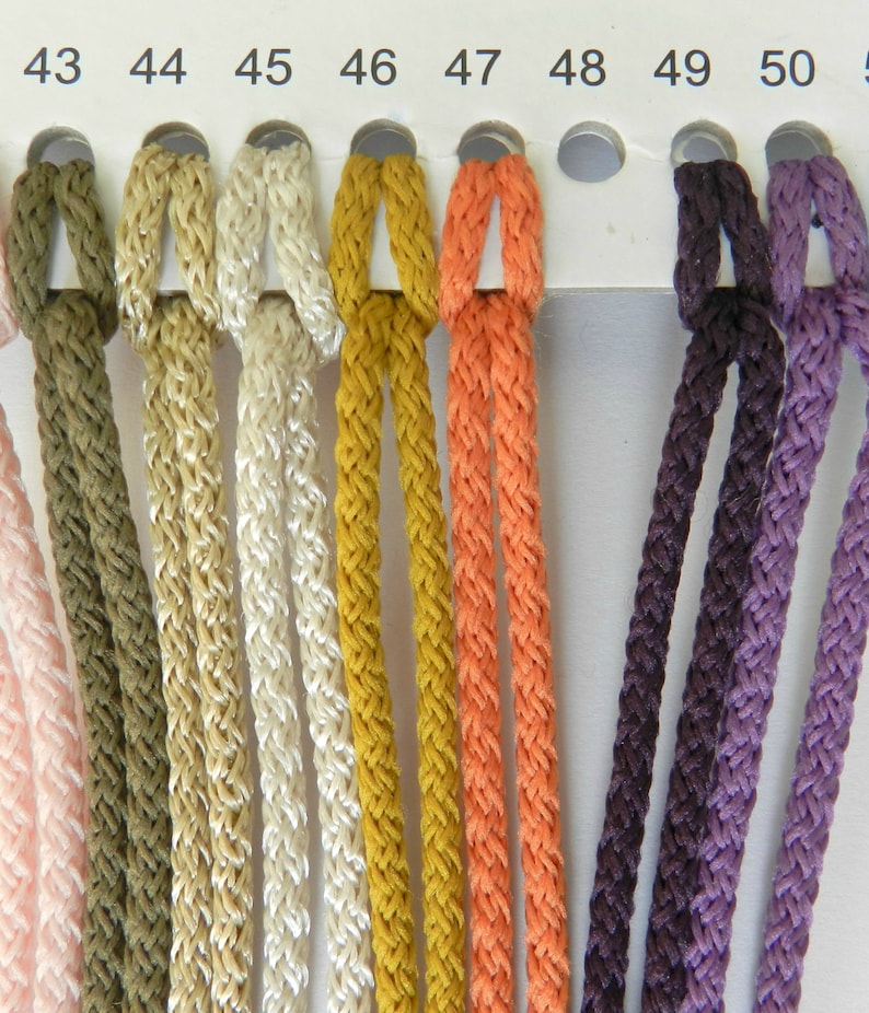 May include: A color chart displaying braided cords in various colors, including olive green, beige, cream, mustard yellow, and orange. The chart also shows cords in shades of purple and brown. Each cord is labeled with a number from 43 to 50.