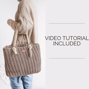 Op de afbeelding: Een bruine gehaakte tote bag met cr&egrave;mekleurige touwhandvatten. De tas wordt gedragen door iemand die een beige trui en een blauwe spijkerbroek draagt. De tekst "VIDEO TUTORIAL INCLUDED" wordt weergegeven op een witte achtergrond.