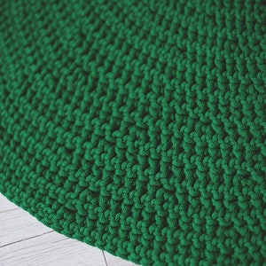 May include: A close-up of a green knitted rug with a textured surface. The rug is made of thick yarn and has a circular shape.