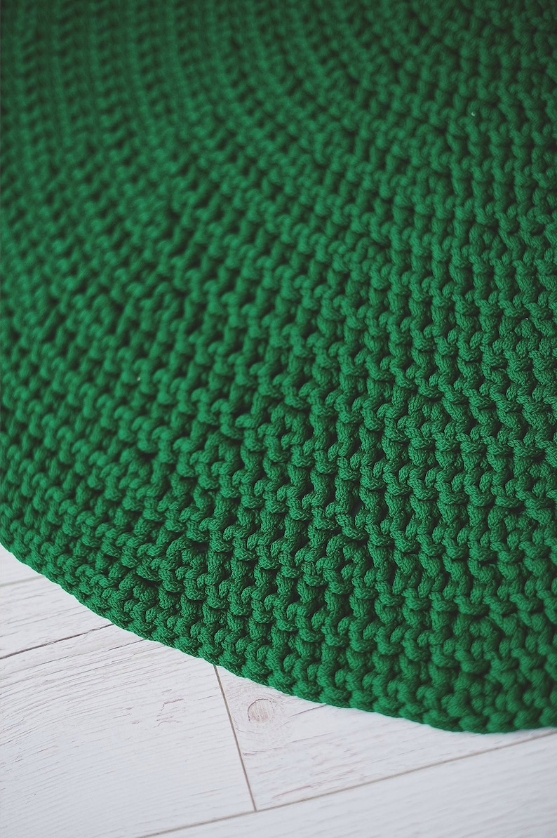 May include: A close-up of a green knitted rug with a textured surface. The rug is made of thick yarn and has a circular shape.