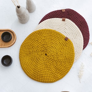 Puede incluir: Tres manteles individuales redondos de crochet en amarillo, crema y burdeos. Los manteles individuales están apilados uno encima del otro.