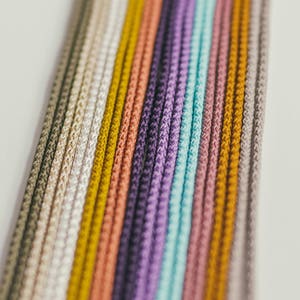 May include: Close-up of a collection of colorful cords in a variety of shades. The cords are arranged vertically, showcasing a spectrum of colors including beige, yellow, peach, purple, and teal. The cords have a textured, woven appearance.