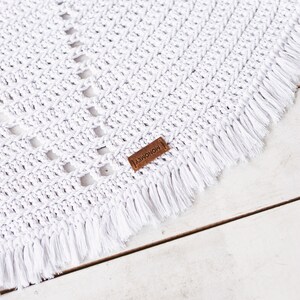 May include: White crocheted throw blanket with a fringe border and a brown leather tag that says "MONOMEY".