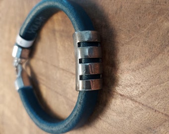 May include: A dark blue leather bracelet with a silver metal bar accent. The bar has three horizontal lines.