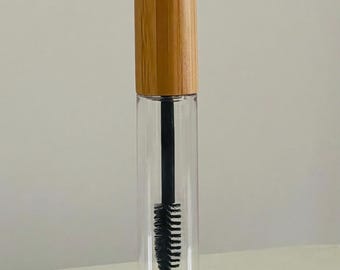 May include: A clear glass bottle with a black mascara wand inside. The bottle has a wooden cap.