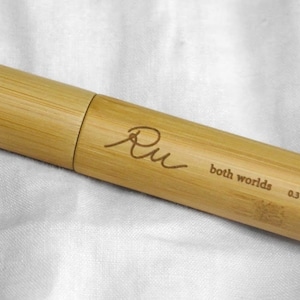 May include: A wooden tube with a bamboo texture and the text "Ru both worlds 0.3 oz" engraved on it.