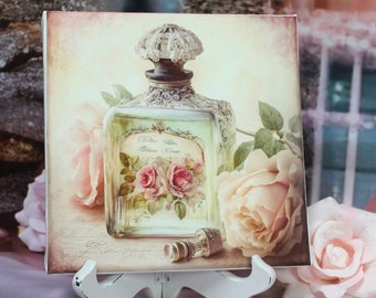 May include: A vintage-style glass bottle with a floral design and the text "Die Gute Alte Zeit" on the label. The bottle is surrounded by pink roses and is displayed on a white easel.