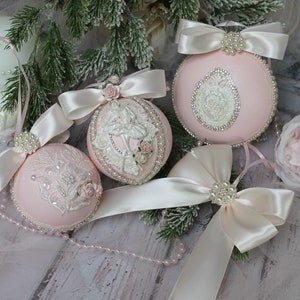 May include: Four pink and white Christmas ornaments with satin bows and pearl accents. The ornaments feature a ballerina, a floral design, and a lace pattern.