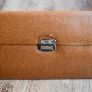 Puede incluir: Un maletín de cuero marrón con un cierre plateado.