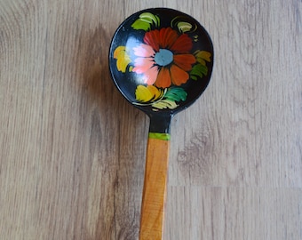 May include: A wooden spoon with a black bowl and a brown handle. The bowl is painted with a colorful floral design.