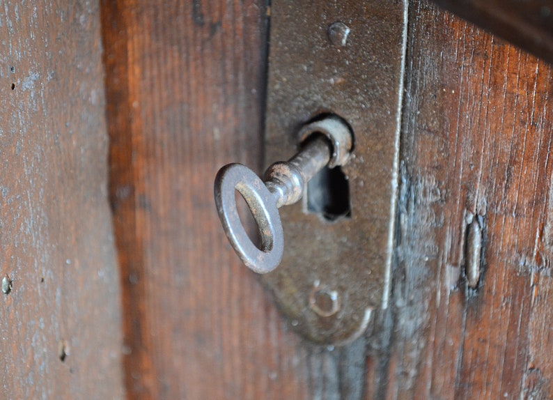 May include: A close-up of a rusty key inserted into a keyhole on a wooden door. The keyhole is surrounded by a metal plate.