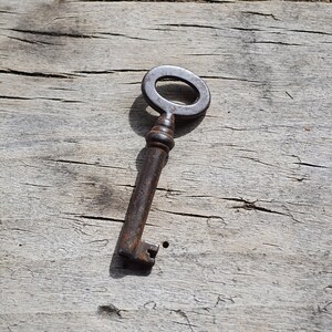 May include: A rusty metal key with a circular head and a long, thin shaft. The key is lying on a weathered wooden surface.