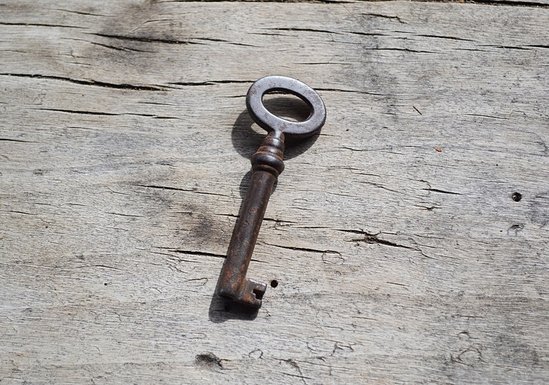 May include: A rusty metal key with a circular head and a long, thin shaft. The key is lying on a weathered wooden surface.