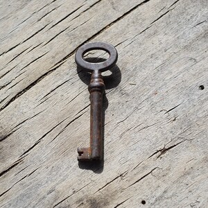 May include: A rusty metal key with a circular keyhole, lying on a weathered wooden surface.