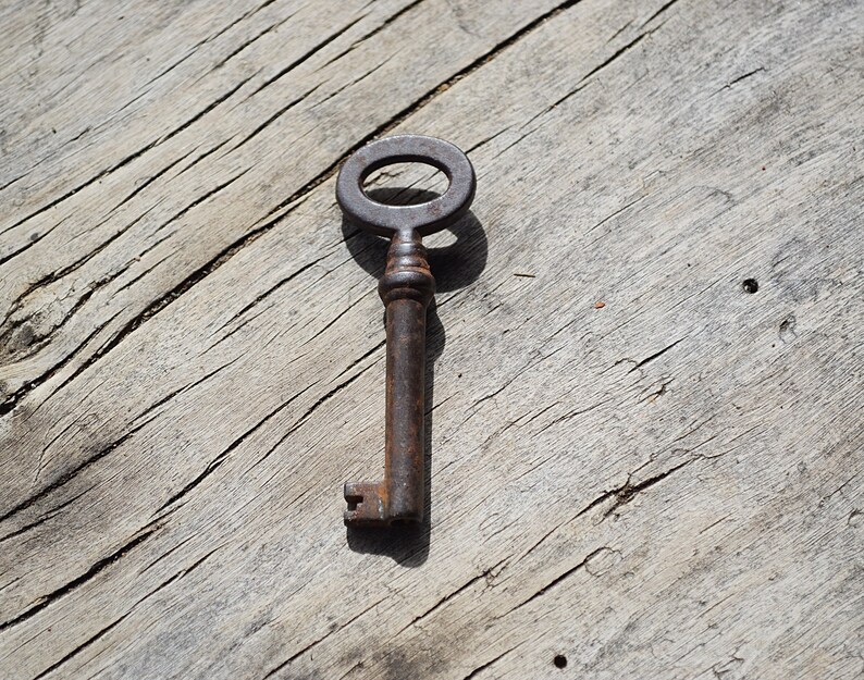 May include: A rusty metal key with a circular keyhole, lying on a weathered wooden surface.