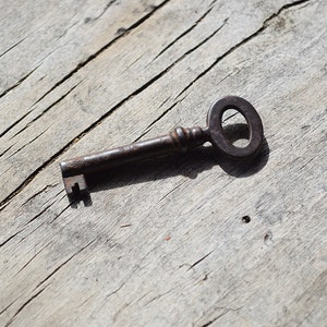 May include: A rusty metal key with a circular bow, lying on a weathered wooden surface.