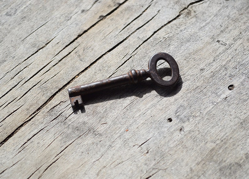 May include: A rusty metal key with a circular bow, lying on a weathered wooden surface.