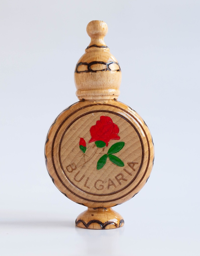 May include: A wooden bottle with a carved top and a round base. The bottle is painted with a red rose and green leaves. The word "BULGARIA" is written around the rose.