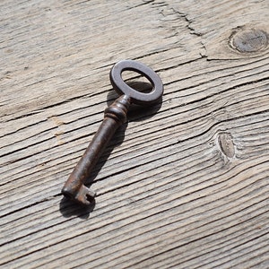 Peut inclure: Une clé en métal rouillée avec un trou de serrure circulaire sur une surface en bois vieilli.