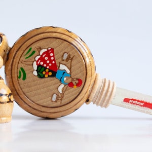 May include: A wooden bottle with a painted design of a woman in a red and white dress. The bottle has a cork stopper and a small glass vial attached to it. The vial is labeled "producer".