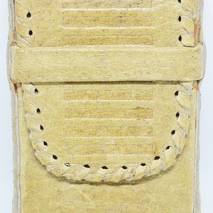 May include: A rectangular, pale yellow leather case with a flap closure. The case has horizontal embossed lines and decorative stitched edges. The flap has a curved, braided trim. The case appears to be vintage or antique.