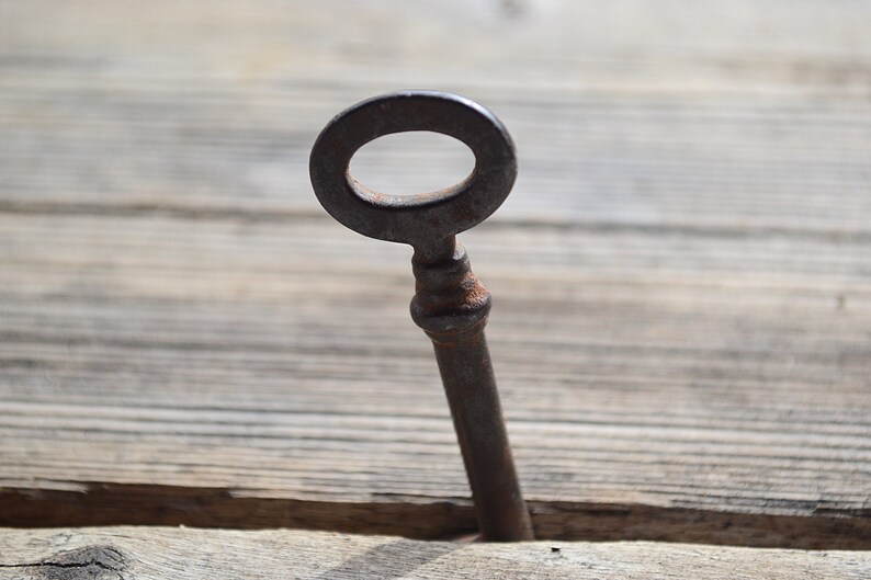 May include: A rusty metal key with a circular head is partially inserted into a wooden surface.