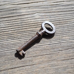 May include: A rusty metal key with a circular head and a long, thin shaft. The key is lying on a weathered wooden surface.