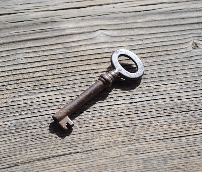 May include: A rusty metal key with a circular head and a long, thin shaft. The key is lying on a weathered wooden surface.