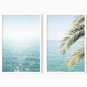 May include: Two framed prints of a beach scene. The left print shows a close-up of sparkling blue water. The right print shows a palm tree frond against a blue sky and ocean.