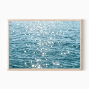 May include: A photograph of a blue body of water with sunlight reflecting off the surface, creating a sparkling effect.