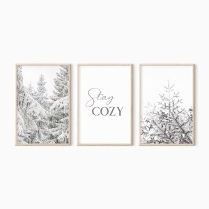 K&ouml;nnte beinhalten: Set aus drei Schwarzwei&szlig;drucken mit schneebedeckten Kiefern und dem Text "Stay Cozy".