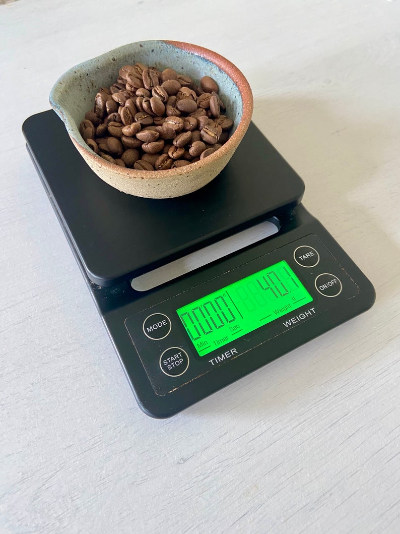 May include: A black digital kitchen scale with a timer and a small bowl of roasted coffee beans on top. The scale displays "0.000" and "40" on the digital display.