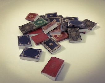 Puede incluir: Una colección de libros en miniatura con cubiertas de varios colores y diseños intrincados. Los libros están dispuestos en una pila sobre una superficie blanca.