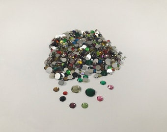 May include: A large pile of assorted colorful round rhinestones, with a smaller scattering of rhinestones in various colors around the pile.