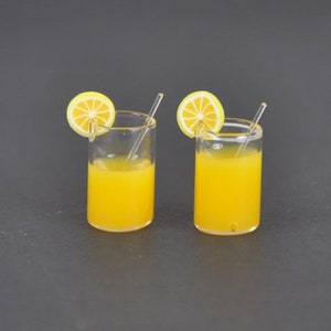 Könnte beinhalten: Zwei klare Glasbecher gefüllt mit Orangensaft und mit einer Zitronenscheibe garniert. Jeder Becher hat einen durchsichtigen Plastikstrohhalm.