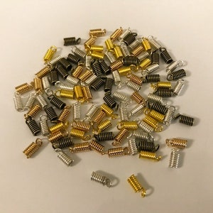 Puede incluir: Un montón grande de cuentas de crimpado de metal dorado, plateado y negro. Las cuentas son pequeñas y cilíndricas con un diseño de resorte.