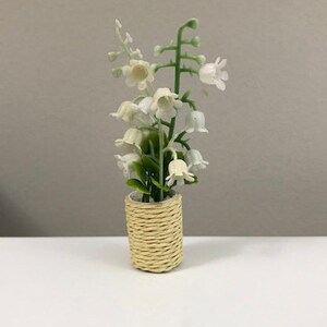 Puede incluir: Un arreglo de flores de lirio blanco en miniatura en una maceta de cesta tejida.