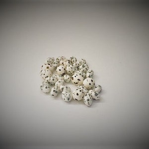 Könnte beinhalten: Nahaufnahme eines Haufens weißer, gefleckter Perlen. Die Perlen sind rund und haben ein geflecktes Muster aus schwarzen und grauen Flecken.