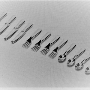 May include: A selection of silver cutlery, comprising knives, forks, and spoons, displayed at an angle on a light background. The polished utensils reflect light, indicating a high-quality finish, suitable for dining.