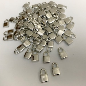 Puede incluir: Un montón grande de dijes de candado de metal plateado. Los dijes son pequeños y detallados, con un diseño clásico de candado.