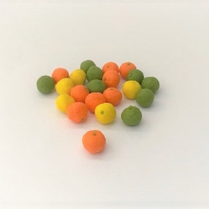Könnte beinhalten: Eine Gruppe von Miniatur-Orangen, Limetten und Zitronen in verschiedenen Grüntönen, Gelb- und Orangetönen. Die Früchte sind auf einer weißen Oberfläche zu einem Haufen angeordnet.