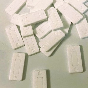 Puede incluir: Una pila de placas de interruptor de luz de plástico blanco con una sola abertura rectangular en el centro de cada placa.