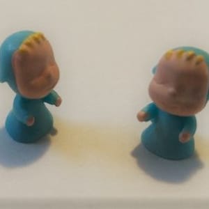 Peut inclure: Deux petites figurines en plastique bleu de bébés endormis avec des cheveux jaunes et des visages roses.