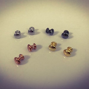 以下が含まれることがあります： 銀、金、黒の小さな丸い金属製のノブの詰め合わせ