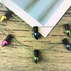 May include: A string of light bulb charms in various colors, including pink, green, blue, and yellow, hanging on a wooden surface.