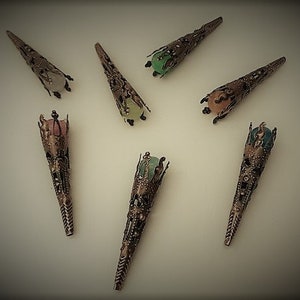 May include: Seven ornate metal cones with different colored glass beads at the top. The cones are a bronze color and have a detailed design.