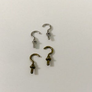 May include: Four metal hooks, two silver and two gold, with a curved hook shape and a pointed end. The hooks are arranged in two pairs, with the silver hooks on top and the gold hooks on the bottom.