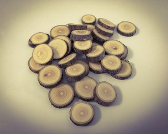 May include: A pile of small, circular wooden slices, each displaying growth rings and bark edges. The natural wood colours vary from light tan to medium brown, offering a rustic appearance. These decorative wood pieces are suitable for crafts and DIY projects.
