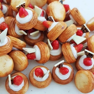 Può includere: Primo piano di un mucchio di pasticcini in miniatura con glassa bianca e guarnizioni di fragole rosse. I pasticcini sono disposti in modo casuale e sono tutti della stessa dimensione.